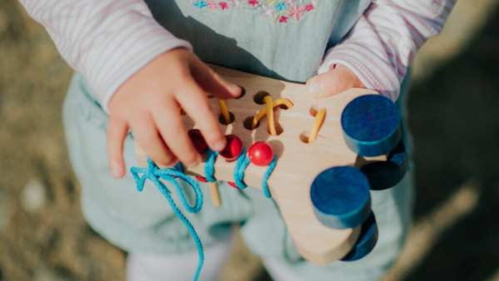 Układanka ma kolorowe sznurówki, trzyma ją dziecko, widać część jego ubioru i małe urocze rączki, jedna trzyma układankę z dołu, druga dotyka sznurówek.