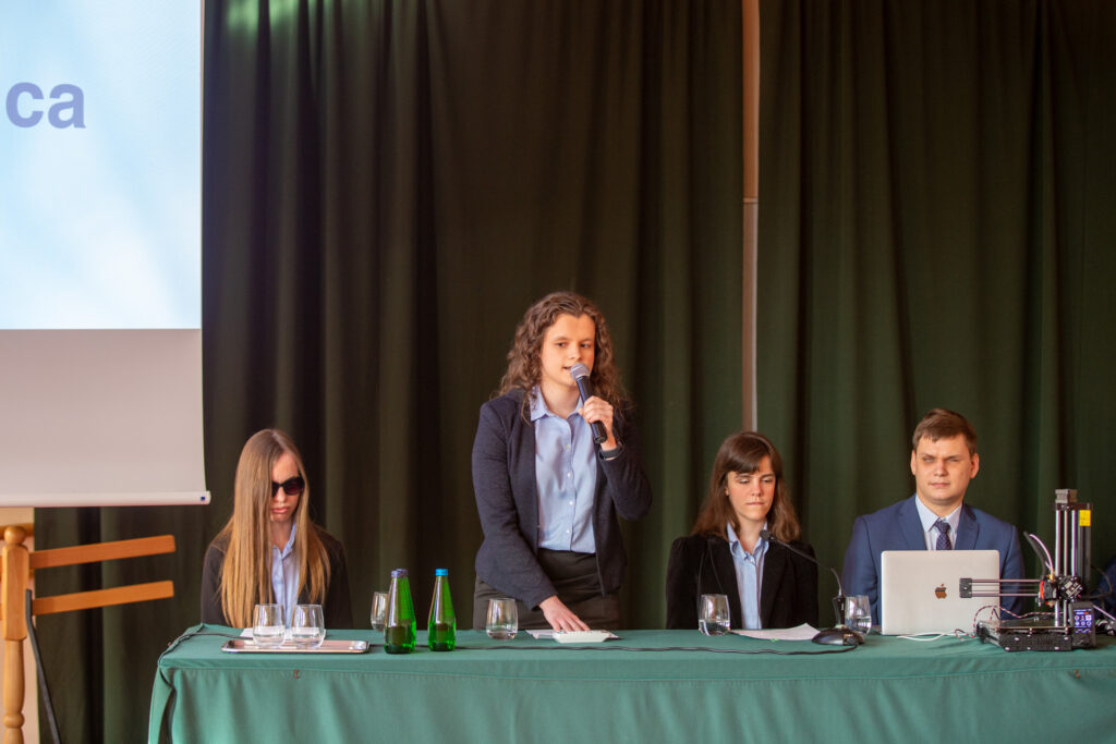 Przy stole znajduje się Zarząd, Julita stoi z mikrofonem.