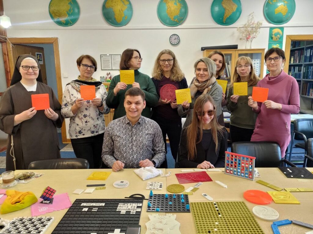 Siostry i nauczycielki Lasek z emotikonami w rękach stoją wokół stołu, Dawid i Monika siedzą przy stole.